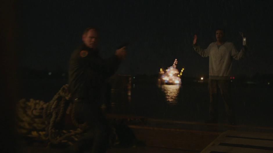Connors points his gun at Billy while the Roxxon rig explodes in the water in the back.