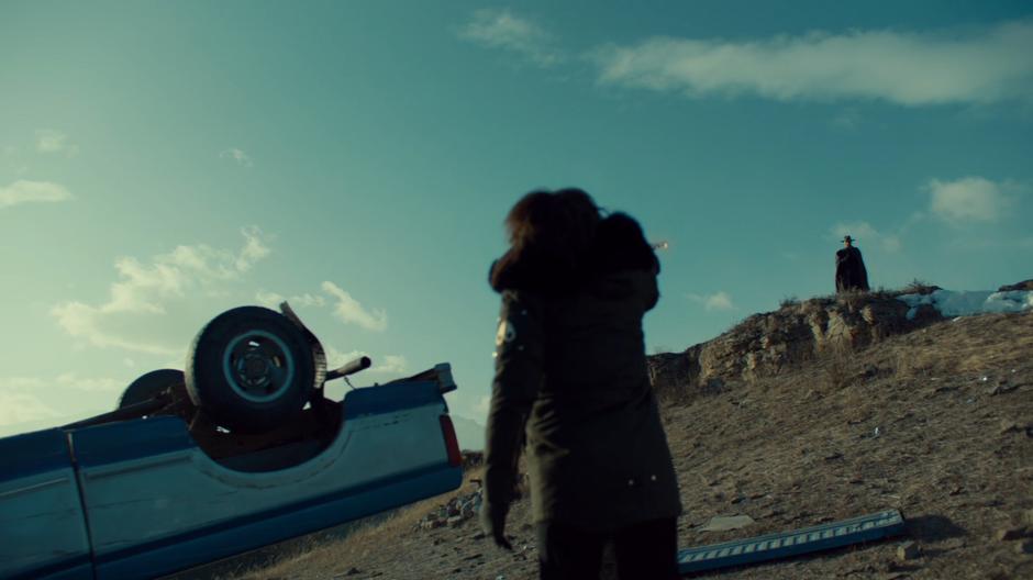 Wynonna points her gun at Bulshar who is standing on the hillside above the crash.