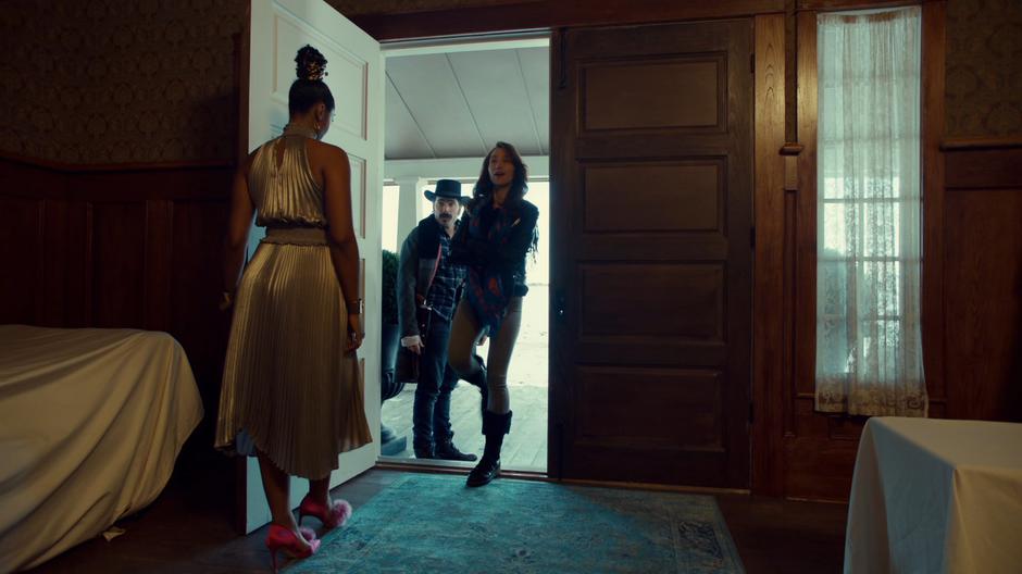 Wynonna saucily steps into the mansion followed by Doc while Kate holds the door open for them.