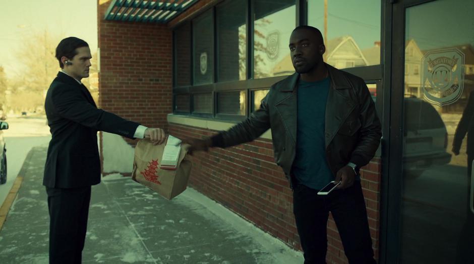 Dolls hands his bag of Chinese food to the Black Badge agent before being escorted away.