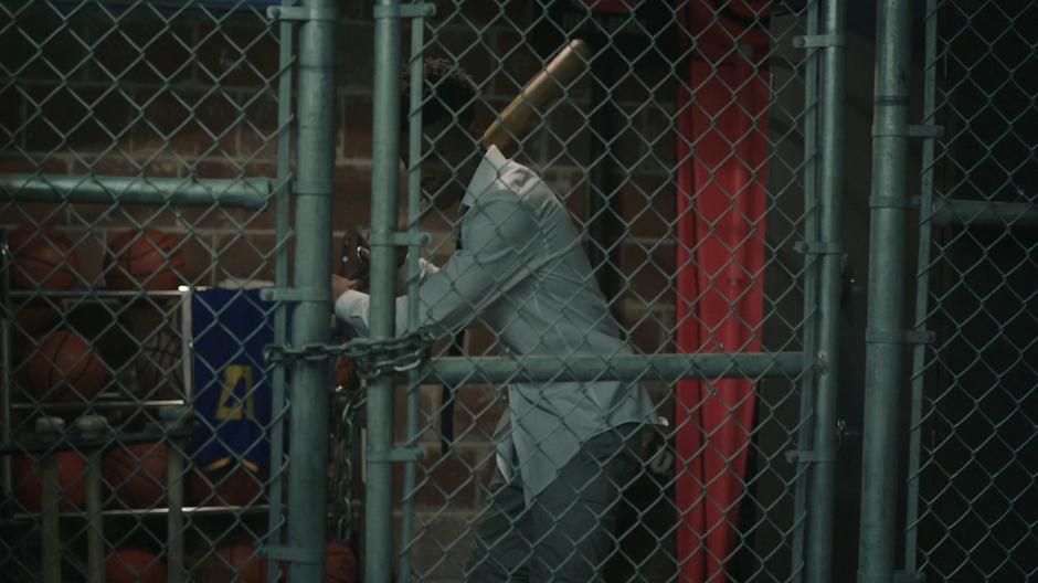 Tyrone swings a bat at the lock on the gate of the storage room he is locked inside.