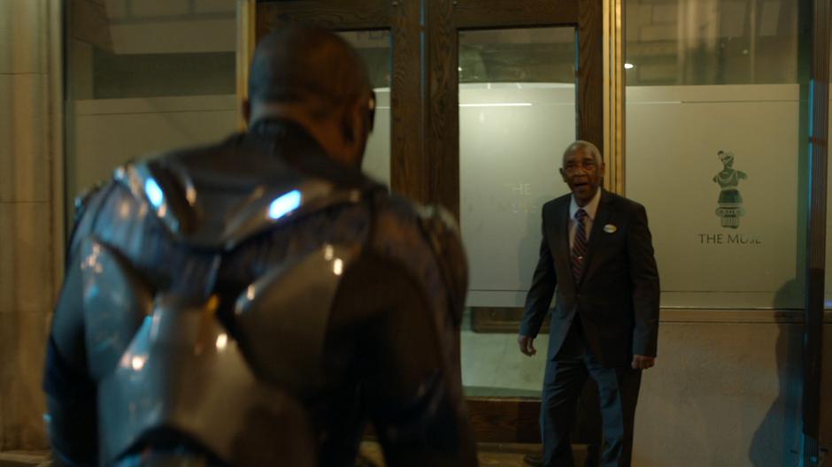 The doorman greets Jefferson as he walks up to the door as Black Lightning.