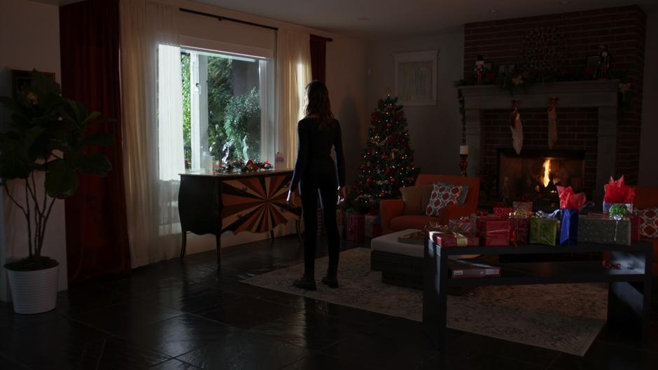Sam stands in the middle of the living room staring out the window while surrounded by Christmas stuff.
