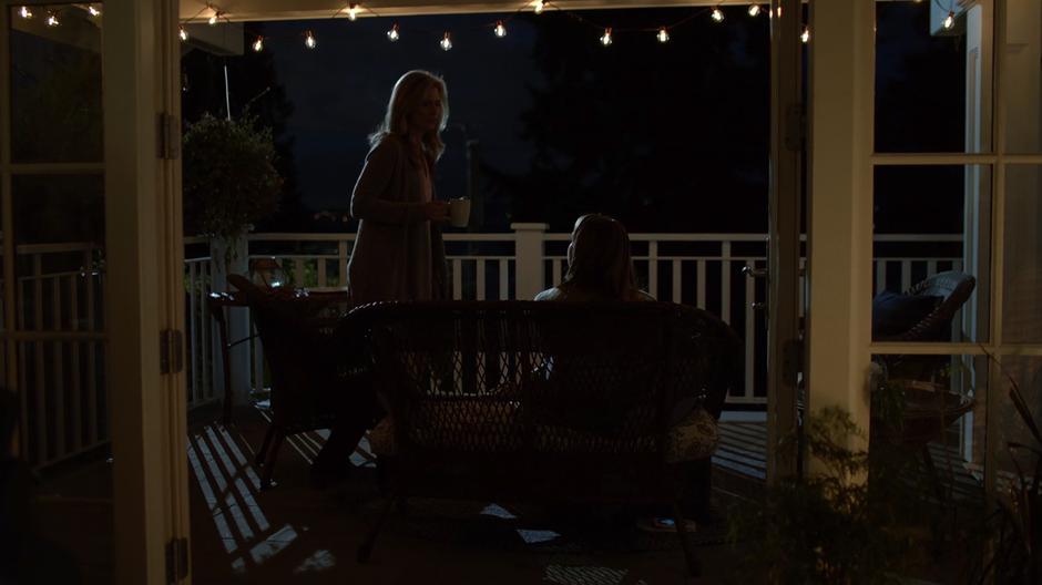 Eliza brings a mug of coffee out onto the porch where Kara is sitting in the evening.
