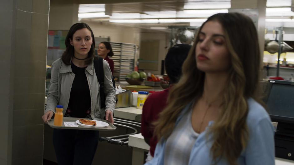 Alex walks out into the cafeteria with her tray of food.