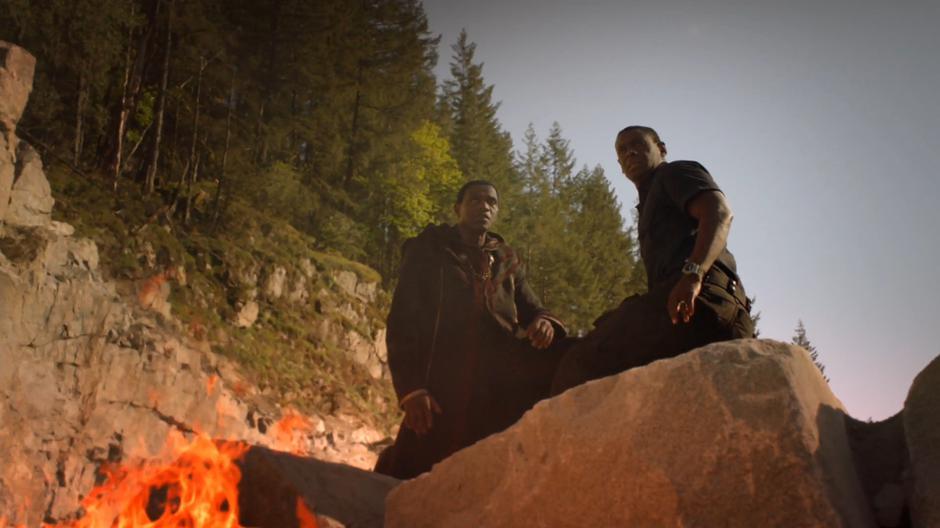 M'yrnn and J'onn kneel on some rocks as the ground breaks apart around them.