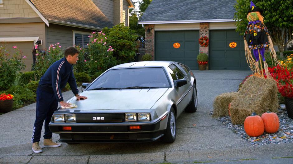 Nate washes a DeLorean in the driveway across the street from the Palmer house.