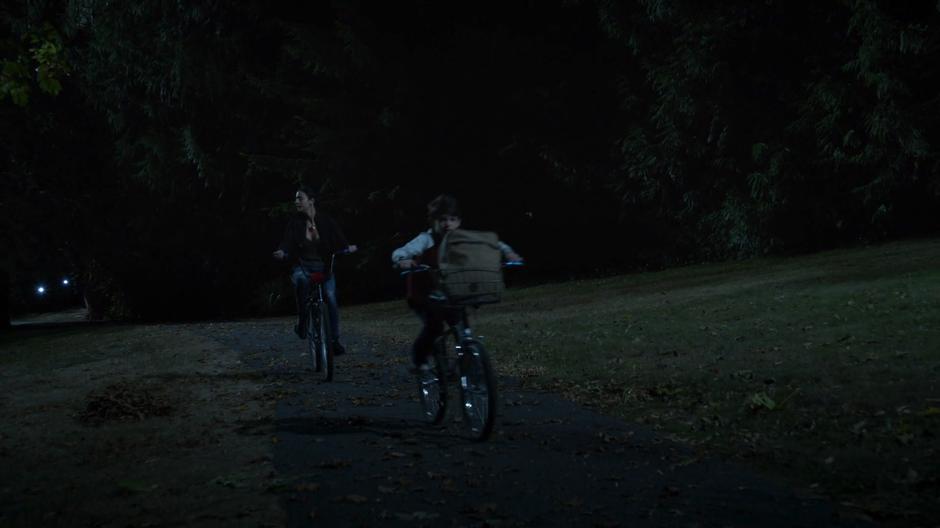Zari and young Ride ride bikes down the path at night.