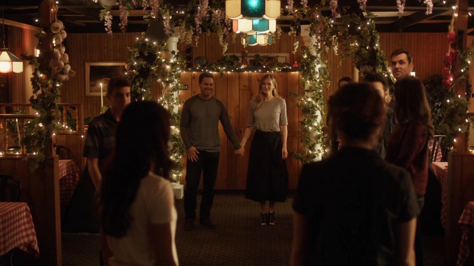 Jack and Emma stand at the front of their friends holding hands as Nina enters with Izzy.