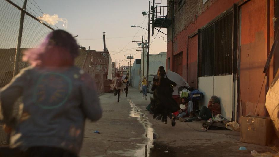 The teens run down the alley near the bus depot past several homeless people.