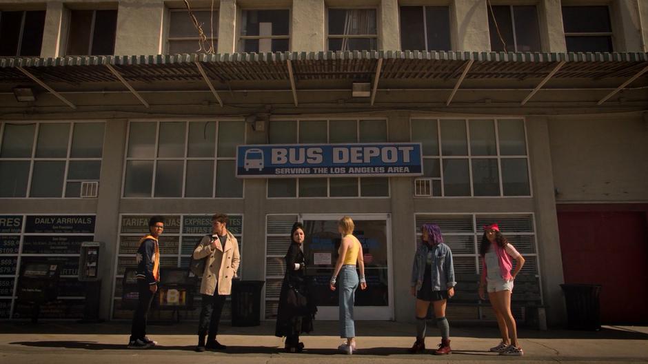 The kids look around while standing in front of the bus depot's office.