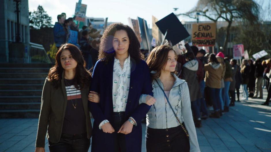 Mel, Macy, and Maggie walk arm-in-arm away from the protest after taking care of Professor Thaine.