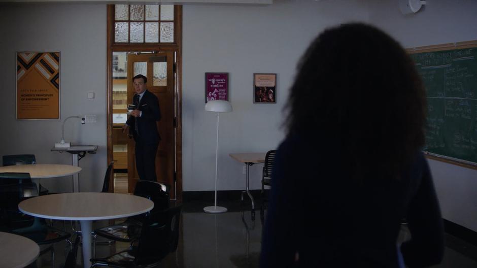 Macy turns as Harry enters the classroom with two cups for tea.