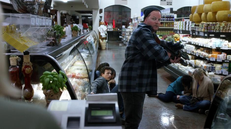 The robber turns back to the cashier as he hold the gun on his hostages.