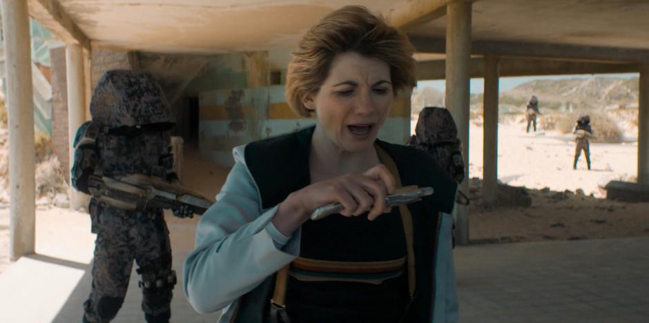 The Doctor turns away from the robotic guards to examine the readings from her sonic.