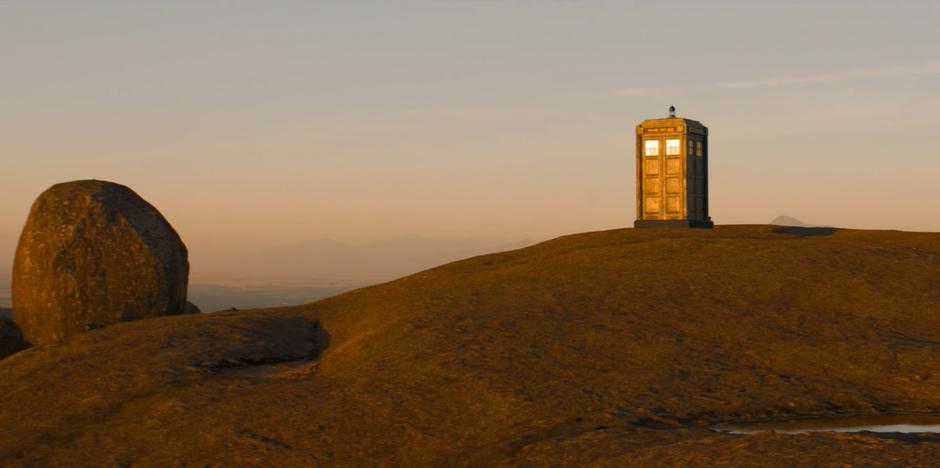 The TARDIS becomes solid on the top of the hill lit by the sunrise.