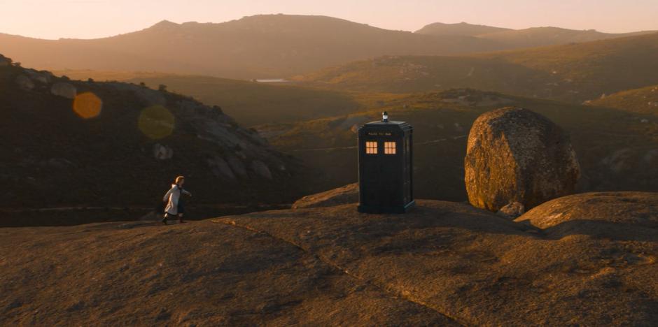 The Doctor strides over to the TARDIS which has just appeared on the hilltop.