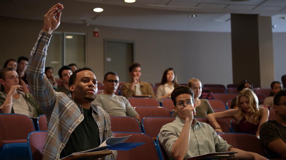 Another student raises his hand to ask a question while the alien student packs up her belongings.