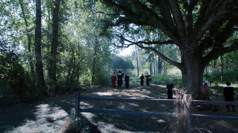 Zari, Ray, and Sara walk out of the woods towards the village while wearing puritan apparel.