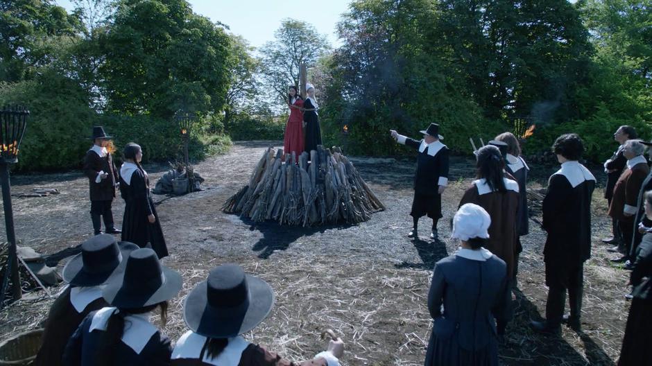 Reverend Parsons points as Zari and Jane Hawthorne who are tied together atop a pyre.