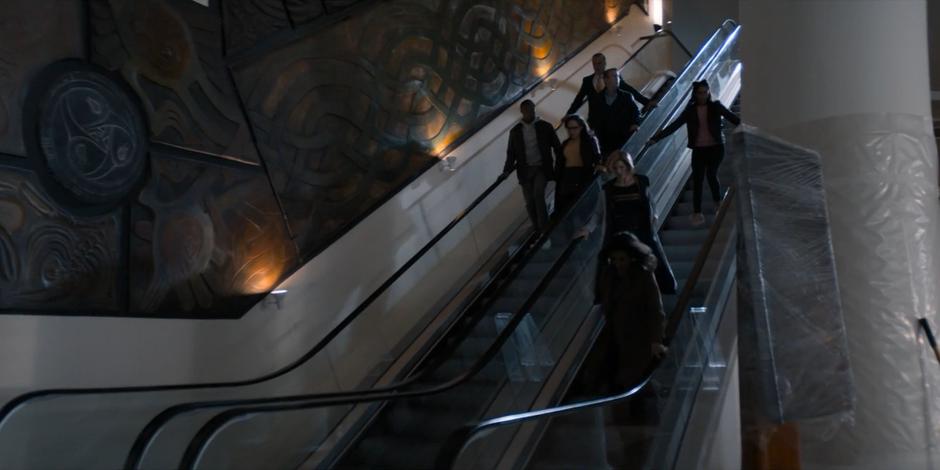 The whole group walks down the stopped escalators towards the exit.