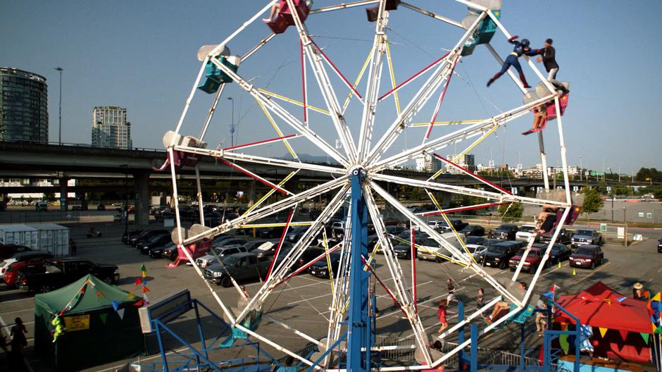 Kara fights the mind-controlled alien to stop him from destroying the ferris wheel.
