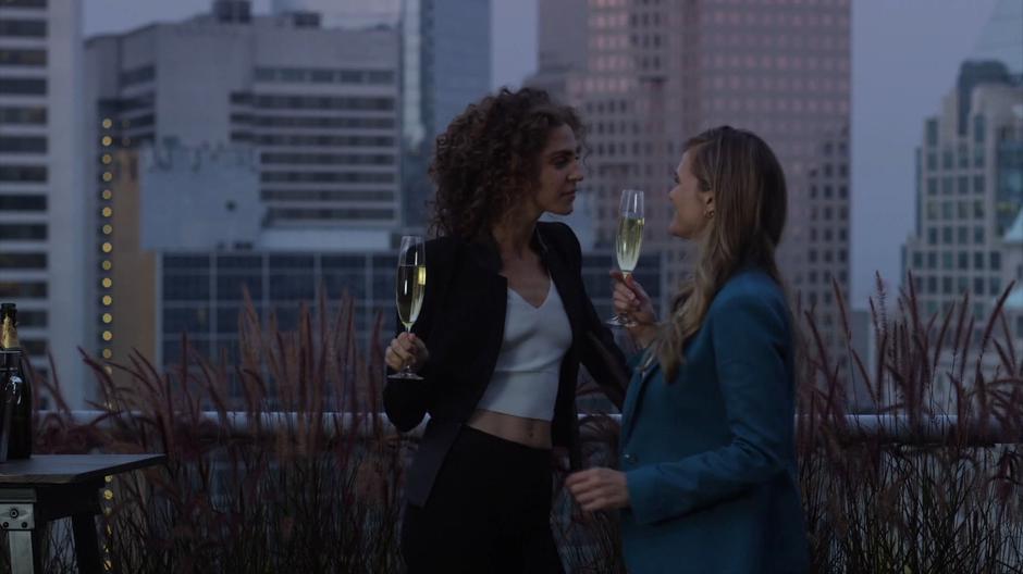 Kylie and Emma stand close on the balcony while drinking celebratory champagne.