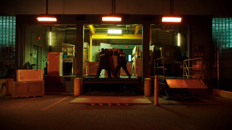 Two security guards attempt to move a crate into the loading dock.