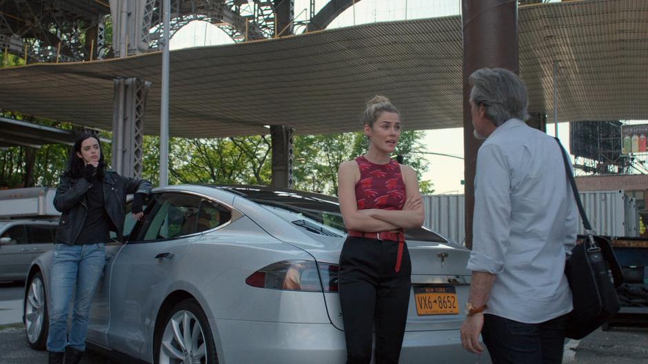 Jessica leans against Max's car while Trish tells him her demands.