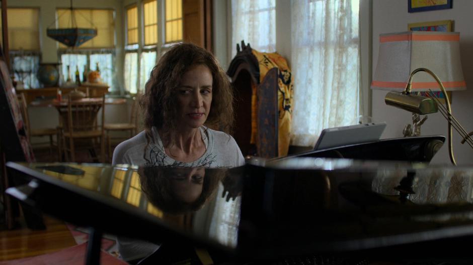 The mysterious woman looks over at her neighbor and her baby from where she is sitting at the piano.