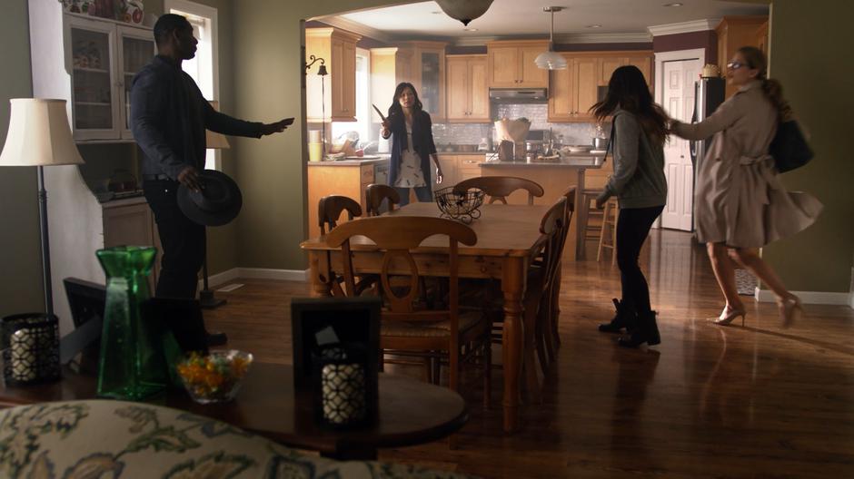 Kara follows Elizabeth Hawkings into the living room while Elizabeth's mother holds a knife at J'onn.