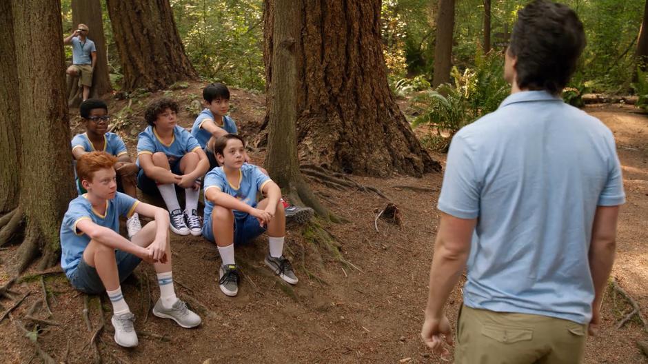 Ray looks past the campers he is attempting to teach to where Constantine is leaning against a tree and drinking.