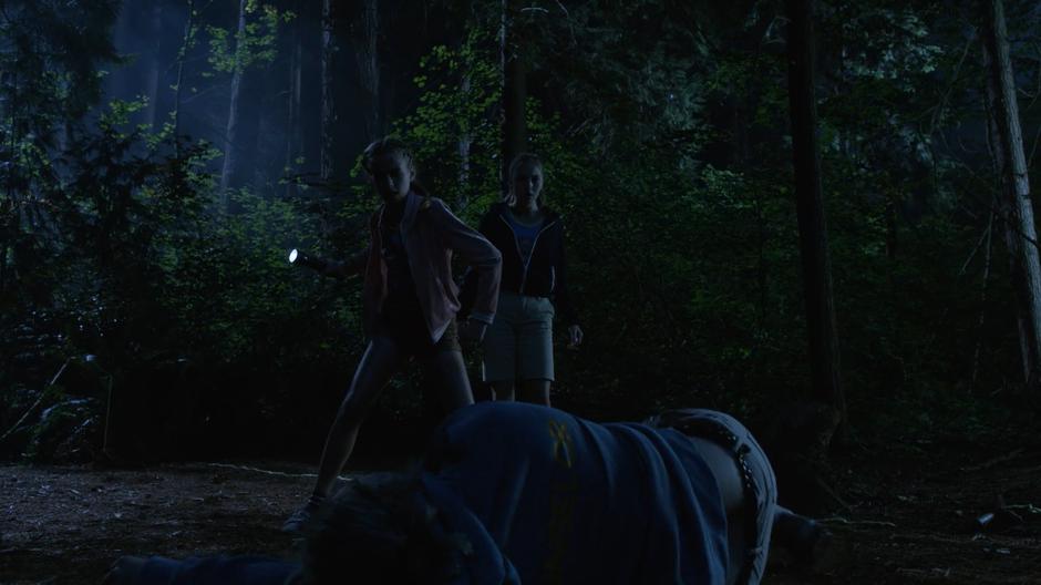 12-year-old Sara and Ava stand over Paula Cooper after knocking her out in the middle of the forest at night.