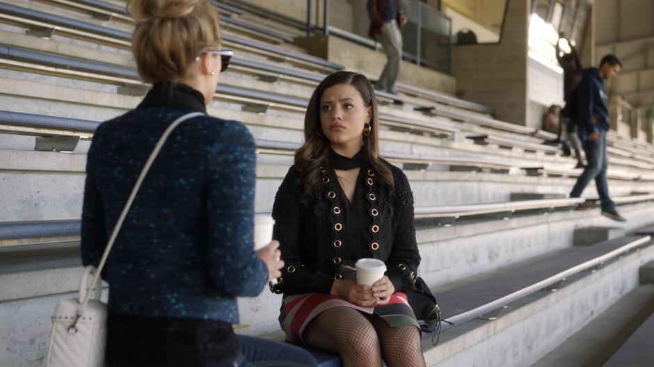 Maggie looks over at Lucy as she sits down next to her on the bleachers.