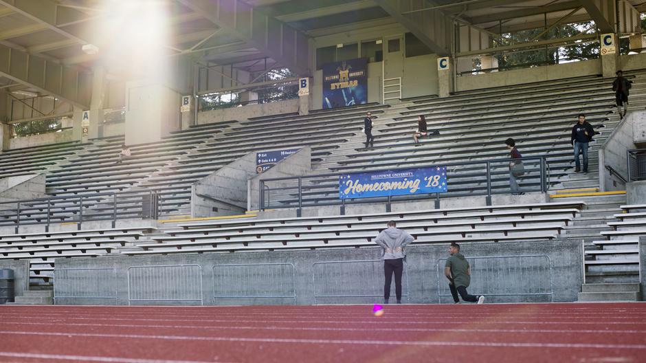 Lucy looks around while walking over to Maggie in the bleachers in the distance.