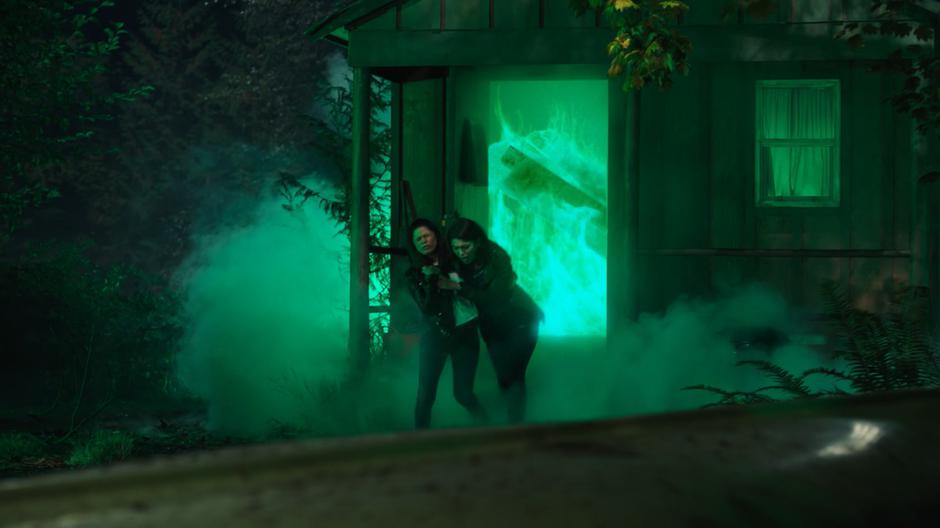 Mel pulls Niko out of the cabin burning with green flames as the roof begins to collapse.