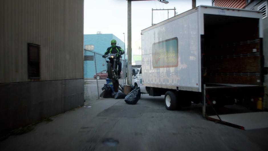 The art thief hops over a pile of debris and past a truck parked across the alley.