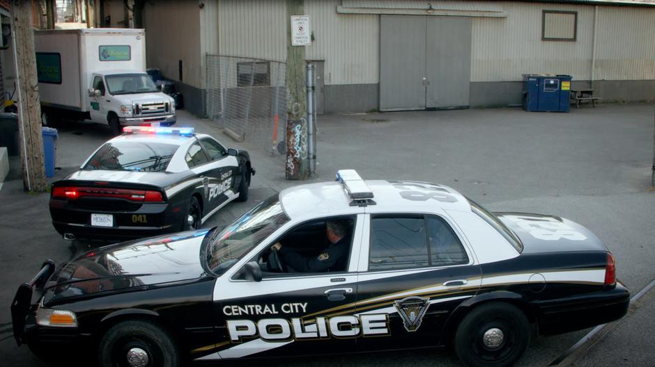 Two police cars find themselves stopped at the end of the alley by the parked van.