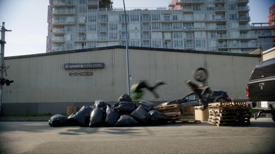 The motorcyclist flips over the stack of pallets and onto a pile of trash bags.