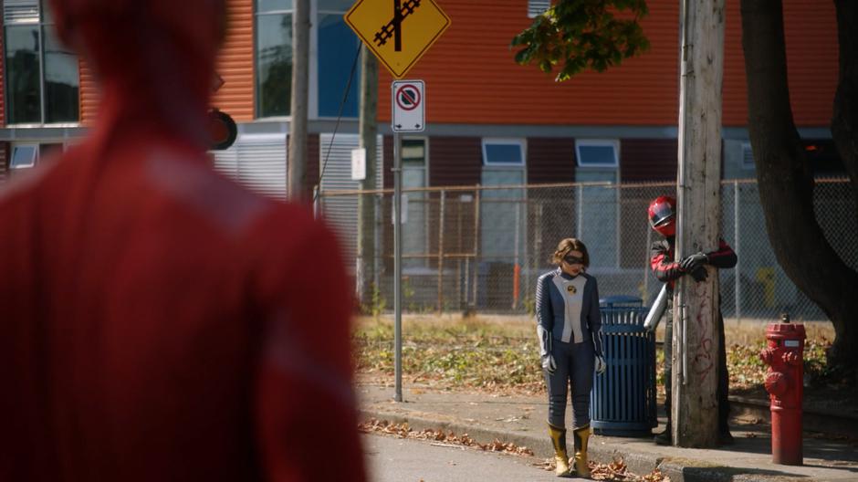 Nora looks down sheepishly while standing next to the motorcyclist she tied to a post.