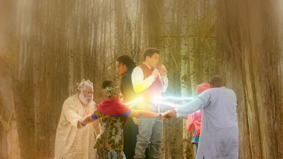 Amaya and Nate stand in the middle of the circle as the elders hold hands surrounding them and beams of light shoot from their totems fire at them.