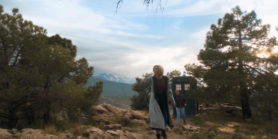 The Doctor scans with her sonic while her friends follow her away from the TARDIS.
