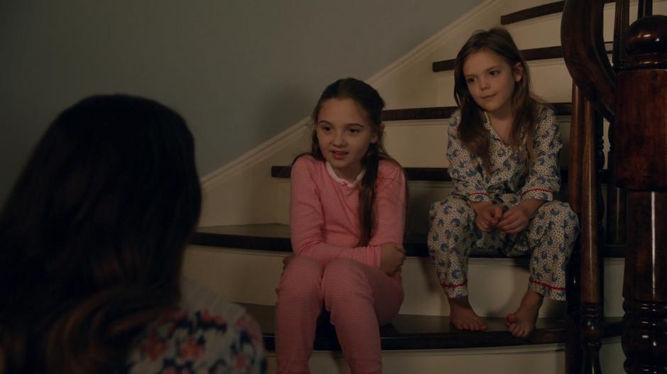 Liza kneels down and talks to Charles's two daughters who are sitting on the stairs.