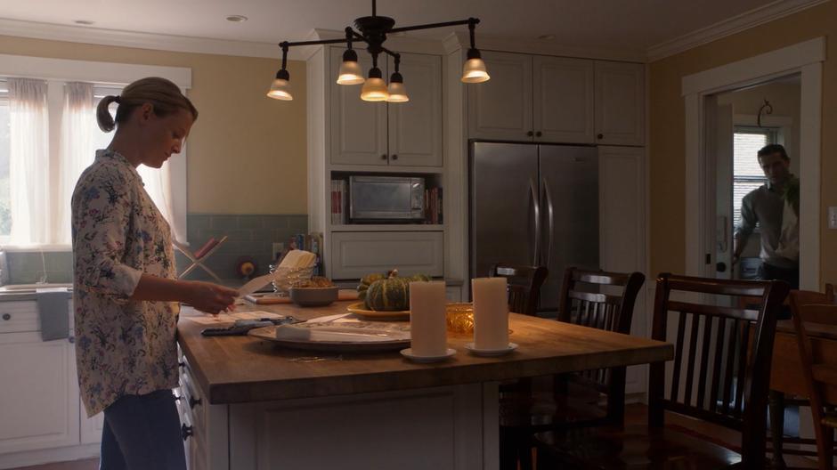 Ben Lockwood walks into the kitchen with a bag of groceries where his wife Lydia is looking over some financial documents.