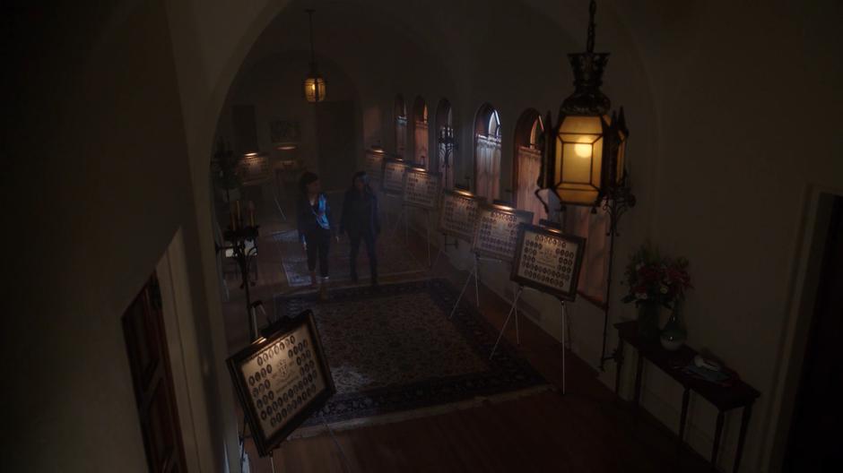 Maggie and Mel walk through the hallway filled with pictures of the past Kappas.