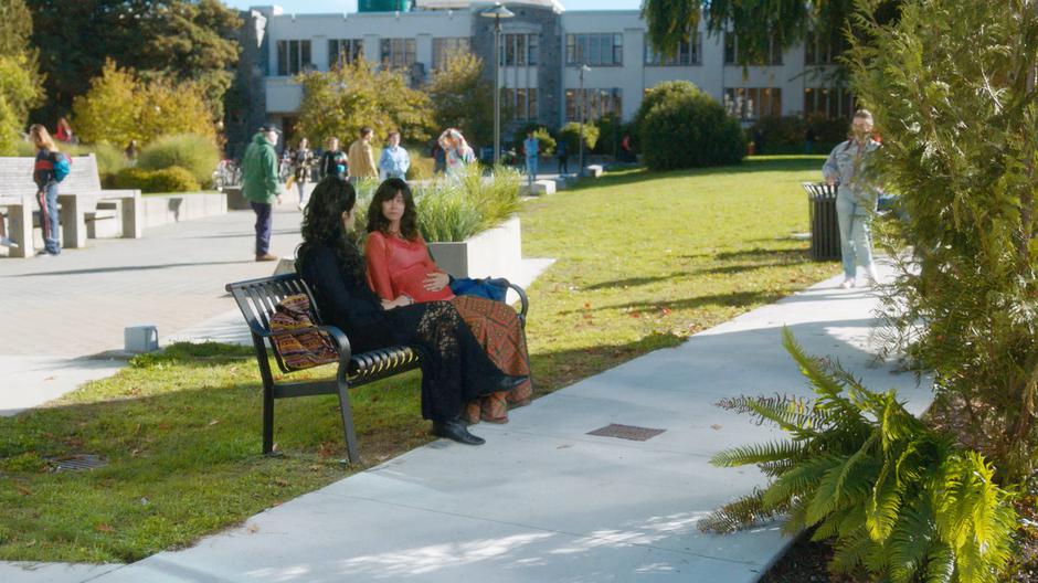 A young and pregnant Marisol sits on a bench talking with her friend.