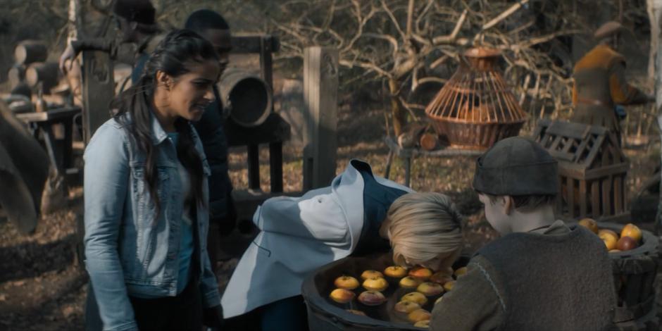 Yasmin watches as the Doctor bobs for apples in the town square.
