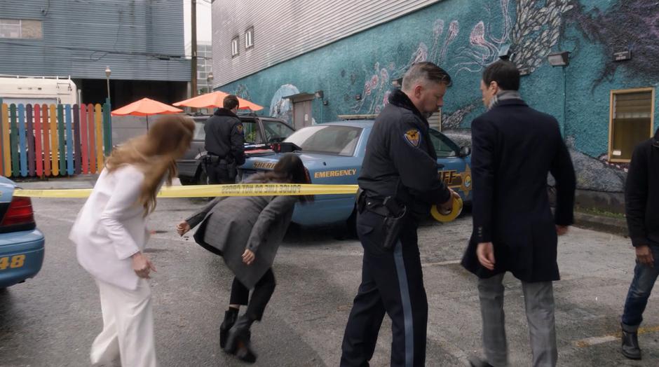 Charity and Mel duck under the police tape while Harry walks around after Mel freezes time.