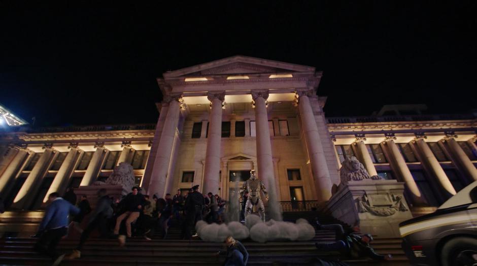 People flee as Amazo lands on the steps of the building.