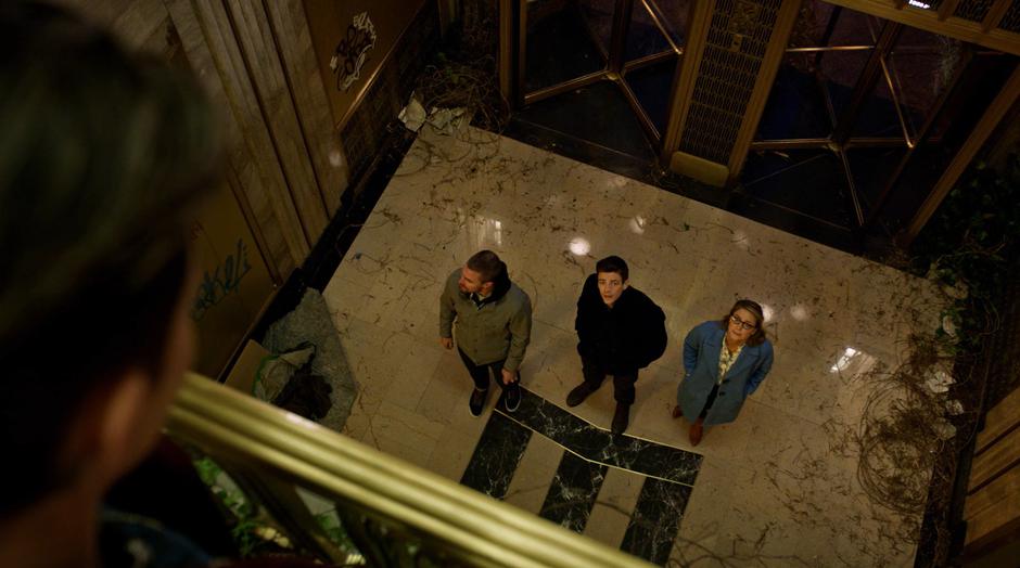 Barry and Kara look up at Kate Kane while Oliver glances around at the trashed lobby.
